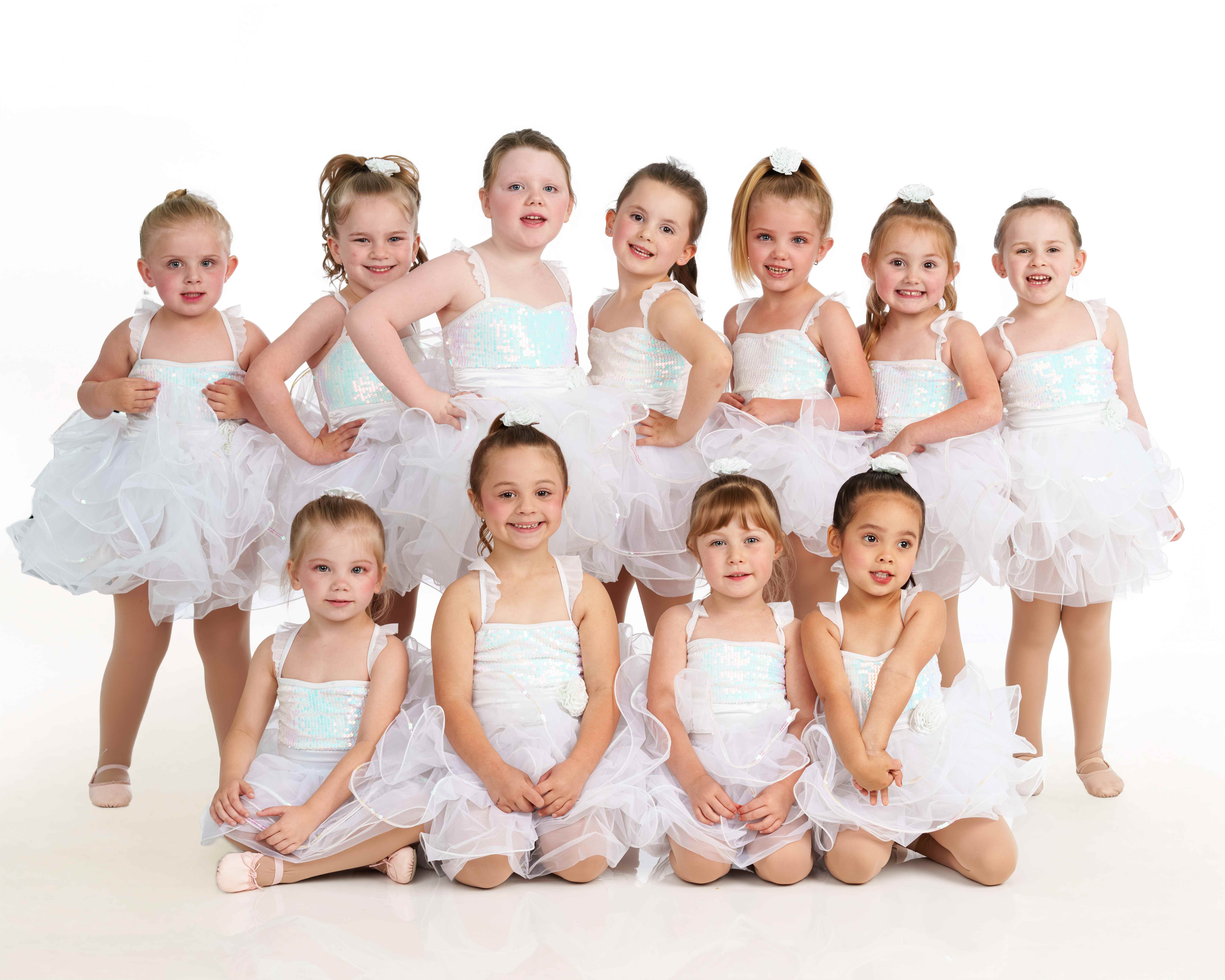 A group of young dancers in white sequined tutus posing together in a bright studio